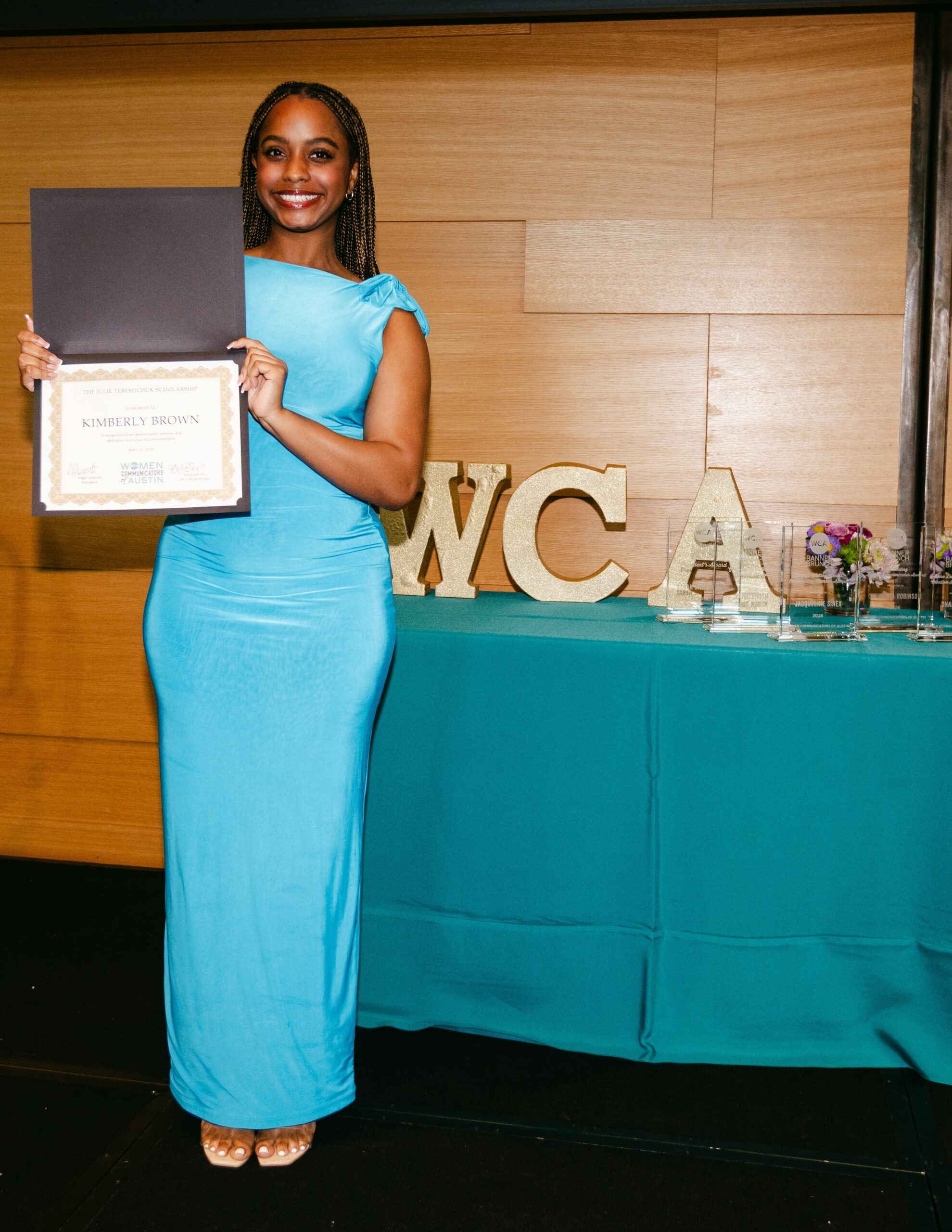 Young woman in blue dress holding an award certificate